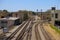 Five sets of railroad tracks near a red brick building with graffiti with railroad traffic signals