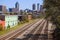 Five sets of railroad tracks surrounded by gravel with colorful buildings along the trees and skyscrapers and office buildings