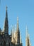 Five of the spires of the Duomo di Milano standing in groups of three and two, tall against blue summer sky