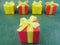 Five square red and yellow gift boxes on green textured background, red one at the front .