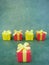 Five square red and yellow gift boxes on green textured background, red one at the front, vertical.