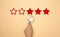 Five stars and a hand with a blue plastic magnifier on a beige background. Evaluation of the quality of services and goods, high