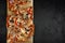 five triangular slices of fresh thin-crust pizza lie in a row on a wooden cutting board on a black concrete background. top view.