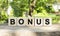 Five wooden blocks lie on a wooden table against the backdrop of a summer garden and create the word BONUS.