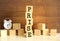 Five wooden cubes stacked vertically to form the word PRISE on a brown background.