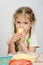 Five-year girl with pigtails eating cheese at table in front of her is a plate of grated cheese