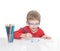 The five-year-old boy in blue points sits at a white table and and draws pencils
