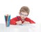 The five-year-old boy in blue points sits at a white table and and draws pencils