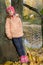 A five-year-old girl stands leaning to a tree on the bank of a pond in an autumn park