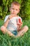 A five-year-old red-haired boy sits in a park on the grass and eats ice cream