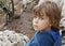 Five years old boy, unhappy look, blue eyes, sitting outdoor on the rock