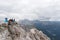 Five young male and female hikers sitting on a mountain peak ledge in the Dolomites and looking at the amazing view