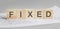 FIXED is written on light wooden blocks. the word is located on a sheet with charts and graphs