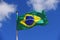 Flag of Brazil waving in the wind in front of a blue sunny sky with clouds.