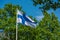 Flag of Finland on a flag pole with gree trees in the background