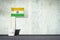 Flag of India, on a stick, in a small bucket, against the background of a concrete wall. Copy space. Signs and Symbols