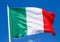 Flag of Italy waving in the wind on flagpole against the sky with clouds on sunny day