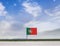 Flag of Portugal with vast meadow and blue sky behind it.