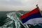 The flag of the Russian Federation flutters in the wind at the stern of the boat against the backdrop of sea waves