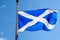 Flag of Scotland Saltire or the Saint Andrew`s Cross blowing in the wind towards clear blue sky in a sunny day