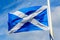 Flag of Scotland Saltire or the Saint Andrew`s Cross blowing in the wind towards clear blue sky in a sunny day