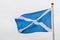 Flag of Scotland Saltire or the Saint Andrew`s Cross blowing in the wind towards cloudy grey sky in a rainy day