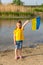 The flag of Ukraine is flying in the hands of a Ukrainian little girl against the backdrop of a lake and reeds