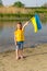 The flag of Ukraine is flying in the hands of a Ukrainian little girl against the backdrop of a lake and reeds