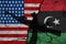 Flag of USA and Libya on textured cracked earth with a silhouette of a machine gun and hand