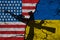 Flag of USA and Ukraine on textured cracked earth with a silhouette of a machine gun and hand