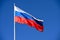 Flagpole with the Russian tricolor flag fluttering in the wind against a blue sky.