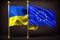 The flags of Ukraine and the European Union fly side by side on a dark background. Symbol of commonwealth, cooperation, mutual