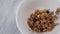 Flakes with pieces of fruit and berries are poured into a white bowl on a wooden table close up.