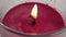 Flame of a red candle flickers in a glass container close-up.