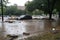 flash flood overtaking city park, with debris and cars floating in the water