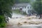 flash flood rushing over riverbank and into neighborhood, with people fleeing the rising water