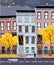Flat cartoon vector illustration of autumn rainy city street. Three-four-story uneven houses, foliage flies. Street cityscape.