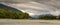 Flat, glacial blue back channel on the Skeena River with dark cloudy and mountains in the background