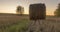 Flat hill meadow timelapse at the summer sunset time. Wild nature and rural haystacks on grass field. Sun rays and green