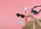 Flat lay of airplane model, sunglasses, camera and  grey credit card in woven bag on pink background. Business and travelling