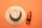 flat lay of beach necessities on vibrant orange backdrop including straw hat and sunscreen lotion