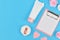 Flat lay with blank clipboard and rose flowers, cream tube in shape of cat, paper hearts and powder puff on blue background with e