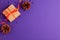 Flat lay of brown gift box with a orange satin ribbon bow and stars shapes pine cone on vibrant purple background with copy space