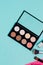 Flat lay of colorful palette of shadows and face corrector blue paper background
