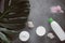 Flat lay composition with white cosmetic products, candle and green leaf on gray concrete background.