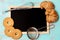 Flat lay design with kitchen utensils, butter cookies/biscuits, croissants and framed blackboard on teal green rustic background,