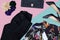 flat lay fashion set of black trausers, floreal shirt, black leather clutch bag, black hills and flower pins over pink and