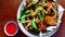 Flat lay of fried wing chicken with crispy kaffir lime leaves and papaya shredded on bowl and chili sauce on brown table.