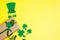 Flat lay green hat, clover leaves or shamrocks on yellow background