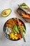 Flat-lay of a homemade vegan poke bowl with tofu, mango, avocado, carrot, edamame, tomato, cucumber and cutting board